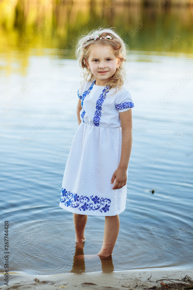 portrait of a little girl who stands in water in a white dress. beach in summer. portrait of a little girl who stands in water in a white dress. beach in summer.