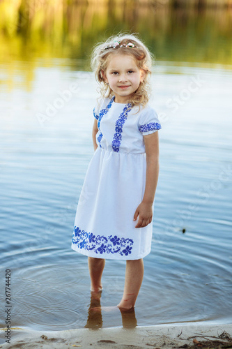 portrait of a little girl who stands in water in a white dress. beach in summer. © Andriy Medvediuk