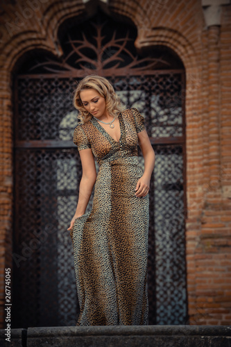 Elegant blonde woman posing against a brick wall wearing a animal print dress.