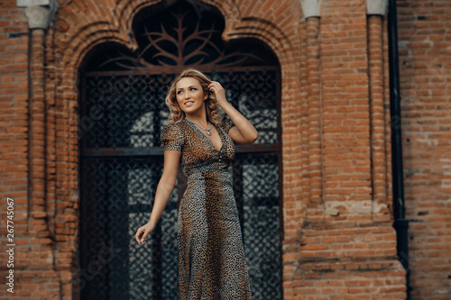 Elegant blonde woman posing against a brick wall wearing a animal print dress. © xpabli