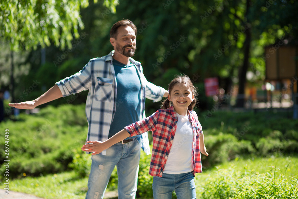 Father Spending Time with Daughter In The Park While Standind Whith Wild Opened Hands And Smiling. Father Spending Time with Daughter In The Park While Standind Whith Wild Opened Hands And Smiling.
