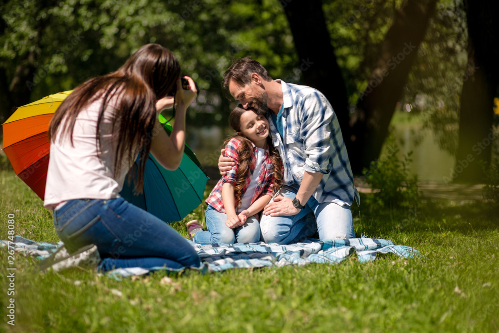 Young Mother Making Photo Of Husband And Daughter In The Park. Young Mother Making Photo Of Husband And Daughter In The Park.