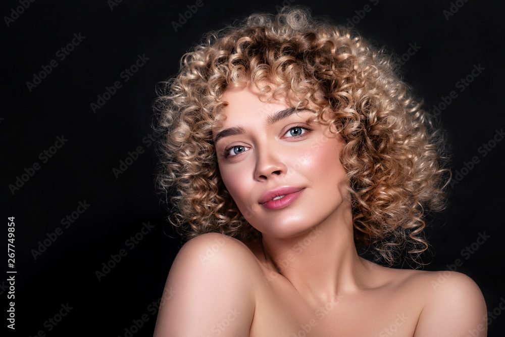 Fototapeta premium Cute caucasian woman with afro (curls) hairstyle on a dark background. She wears nude make up
