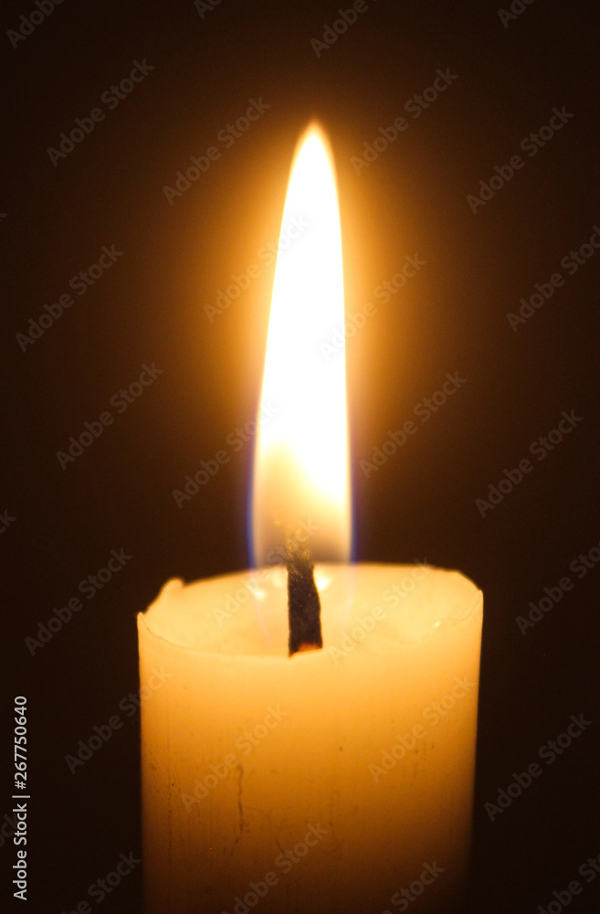 Flame of one white burning brightly wax candle on the dark black background . Mourning candle. Candle flame Flame of one white burning brightly wax candle on the dark black background . Mourning candle. Candle flame