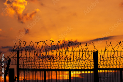 Barbed wire fence on the background of a fiery, bright sunset.
