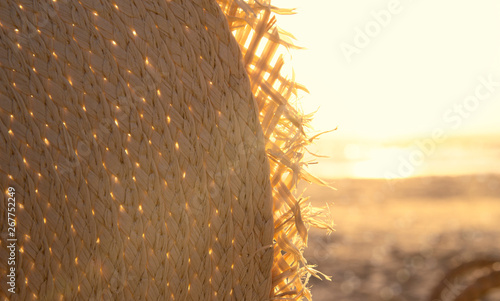 Fragment of a straw hat in sunset light on the beach. Vacation theme concept. Summer holiday background