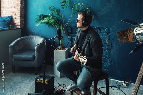 Man singer sitting on a stool in a headphones with a guitar recording a track in a home studio photo