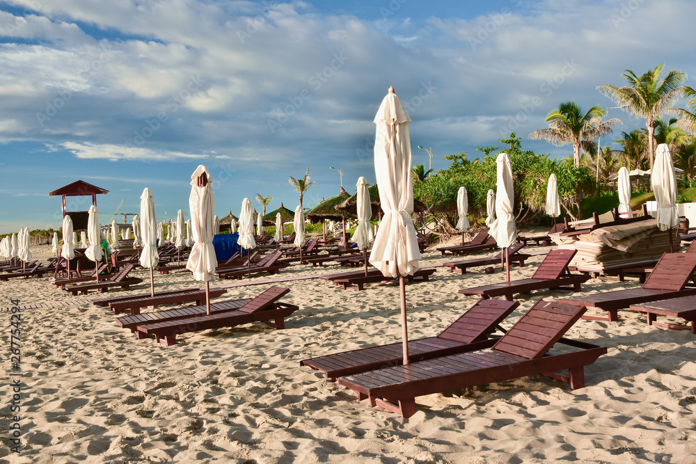 Sun loungers and umbrellas on an empty sandy beach. Summer sunny cloudy blue sky. Kamran. Vietnam.