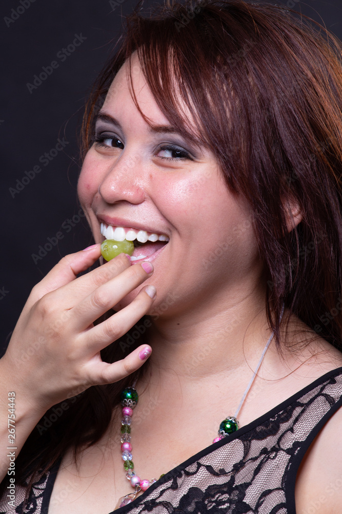Young latina hispanic woman smiling while eating a grape Young latina hispanic woman smiling while eating a grape