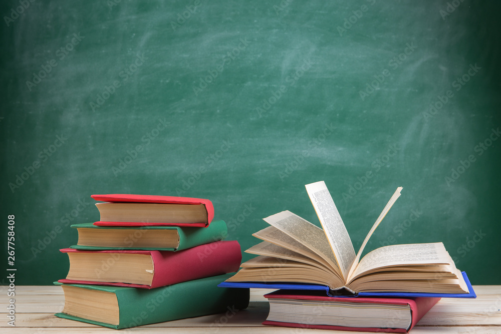 Education and reading concept - group of colorful books on the wooden table in the classroom, blackboard background Education and reading concept - group of colorful books on the wooden table in the classroom, blackboard background