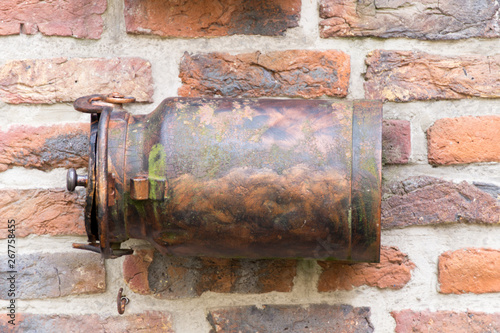 old rusty milk barrel, can, used as mailbox against brick wall