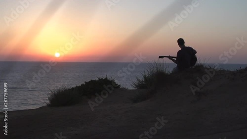 Silhouette of young man songwriting outdoors playing acoustic guitar at sunset photo