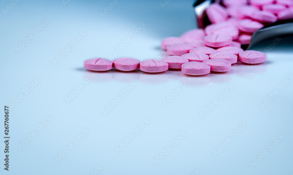 Pink tablets pills on blurred background of drug tray. Pharmaceutical industry. Pharmacy products. Vitamins and supplements. Medication use in hospital or drugstore. Global drug retail market. Pink tablets pills on blurred background of drug tray. Pharmaceutical industry. Pharmacy products. Vitamins and supplements. Medication use in hospital or drugstore. Global drug retail market.