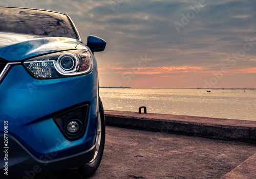 Blue compact SUV car with sport and modern design parked on concrete road by the sea at sunset in the evening. Hybrid and electric car technology concept. Car parking space. Automotive industry. © Artinun