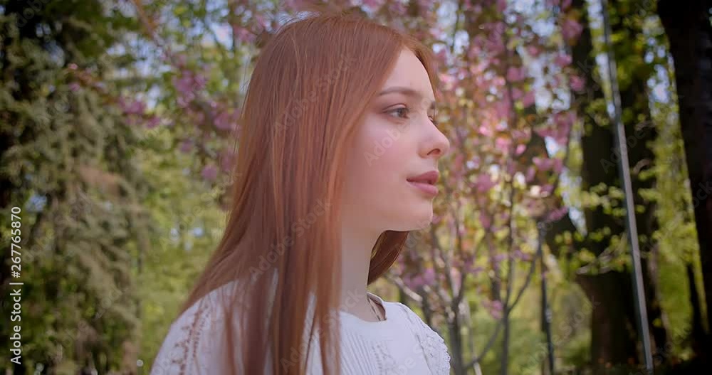 Ginger girl in white blouse walking along at pink floral garden and smiling into camera prettily. Ginger girl in white blouse walking along at pink floral garden and smiling into camera prettily.