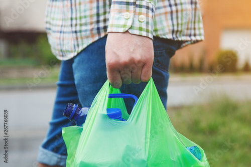 waste management, man's hand carrying green plastic bag full of plastic bottles ready for recycling, copy space