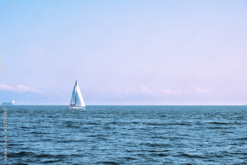 Luxury yacht with white sails in open sea at beautiful sunny day. Small waves on the sea and white clouds on horizon line. Weekend getaway from city. Wonderful world. Natural background. 