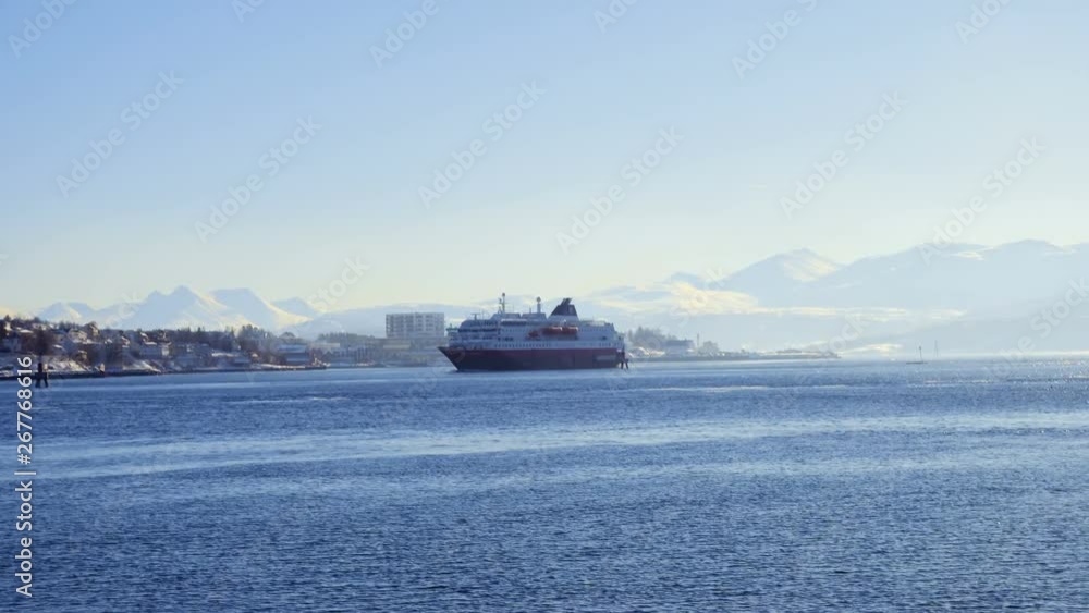 FINNSNES, TROMS, NORWAY, MARCH 11 2019: cruise service vessel Hurtigruten going along winter fjord shore at sunny day FINNSNES, TROMS, NORWAY, MARCH 11 2019: cruise service vessel Hurtigruten going along winter fjord shore at sunny day