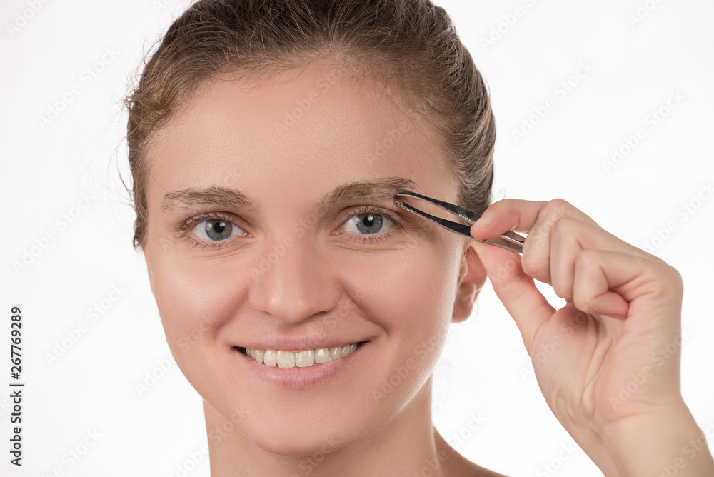 Young girl pulls out her eyebrows with tweezers metal on a white background Young girl pulls out her eyebrows with tweezers metal on a white background