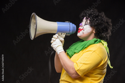 Scary clown shouting into a megaphone on a black background