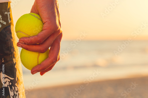 Hand holding two tennis balls on the beach at sunset © Juanrastock