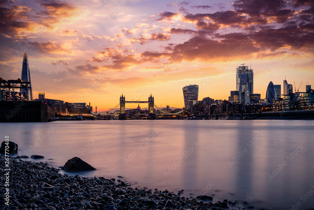 Blick vom Ufer der Themse auf die Skyline von London, Großbritannien, mit der Tower Brücke und der City bei Sonnenuntergang