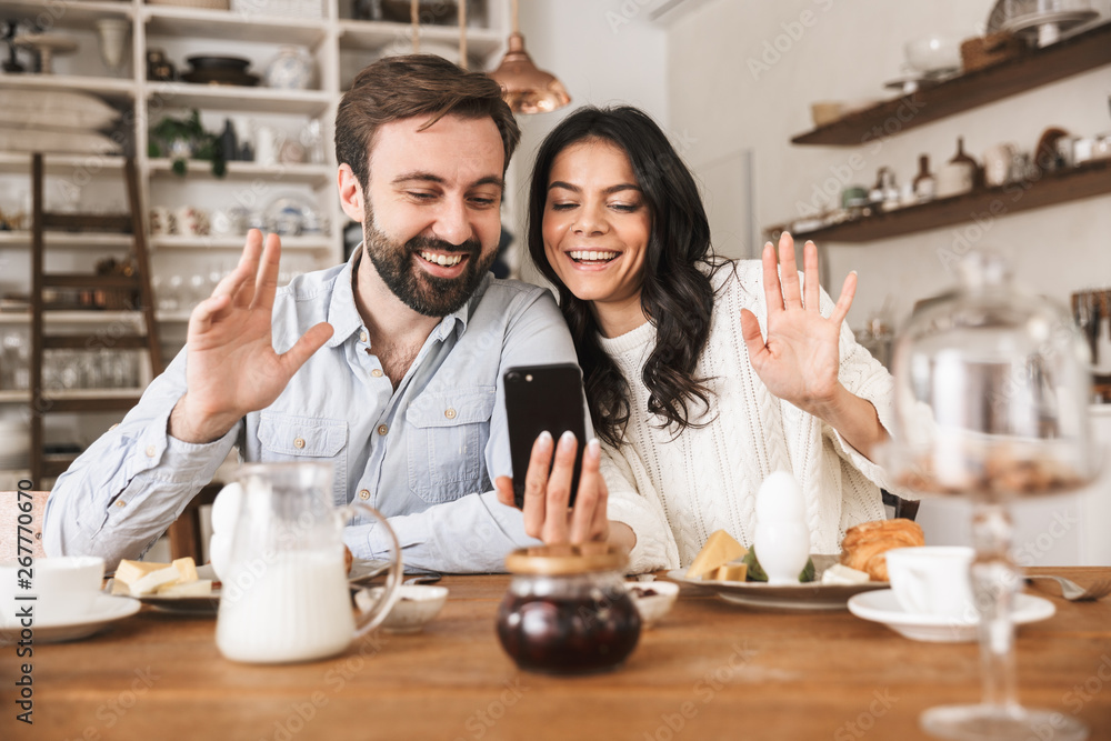 Portrait of smiling european couple using smartphone while having breakfast in kitchen at home Portrait of smiling european couple using smartphone while having breakfast in kitchen at home