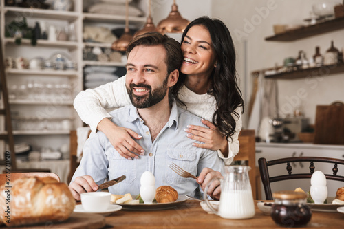 Portrait of modern european couple eating at table while having breakfast in kitchen at home