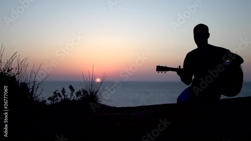 Cinematic Silhouette of young man outdoors playing acoustic guitar at sunset