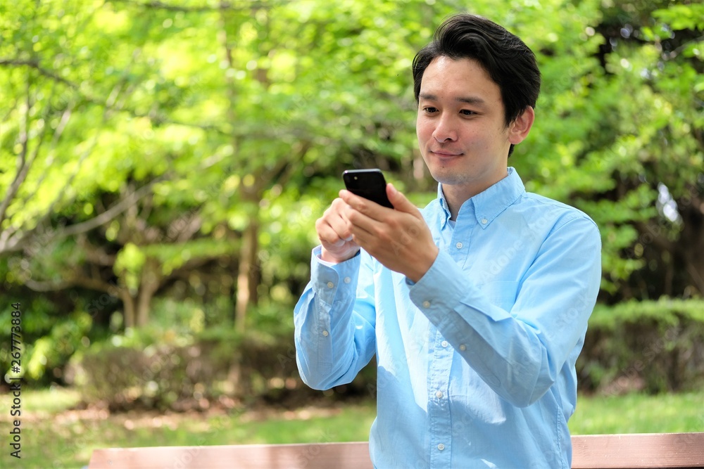 公園でスマホ 携帯を操作する三十代男性 公園でスマホ 携帯を操作する三十代男性