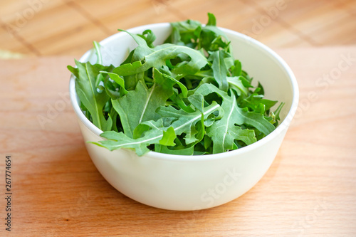 Fresh healthy green arugula leaves in a white bowl on light wooden background.