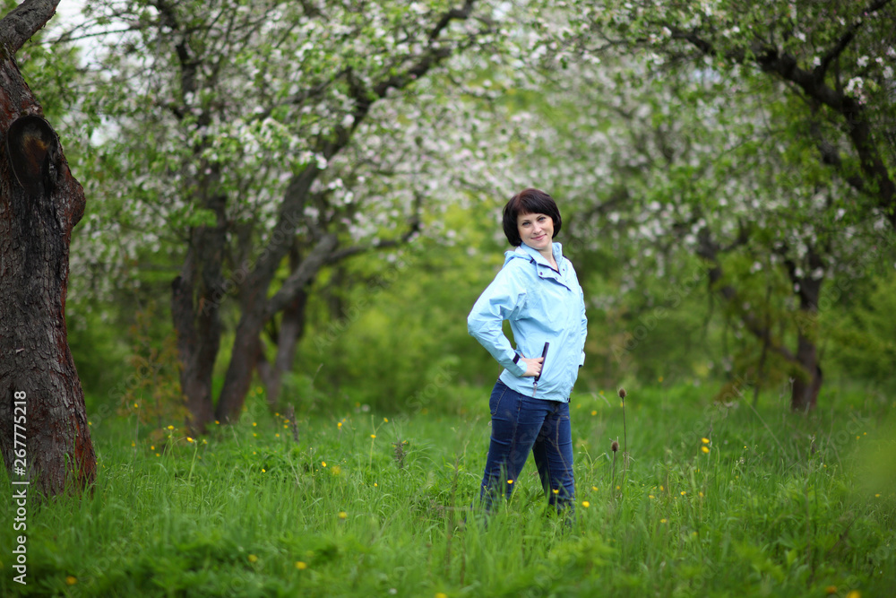 Beautiful mature woman posing for the camera in the spring garden. The girl enjoys the flowering of apple trees.