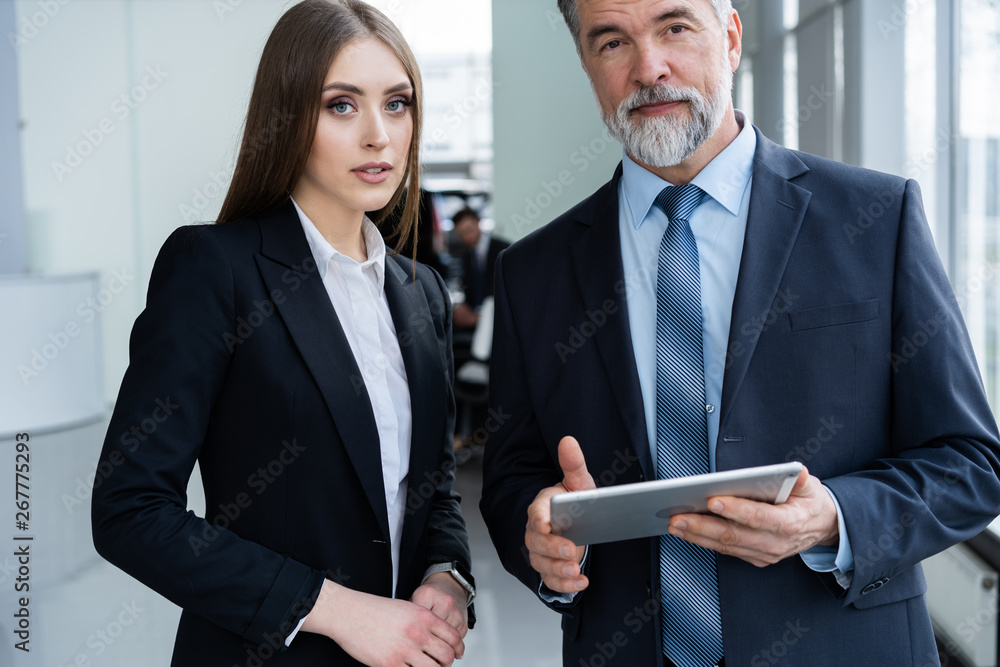 © opolja - Business People standing in the office and looking at a tablet.