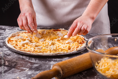 young woman in a gray aprons prepares a Hawaiian pizza