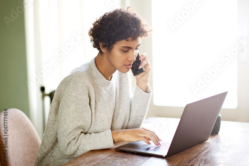 young african americna woman talking on mobile phone and looking at laptop photo