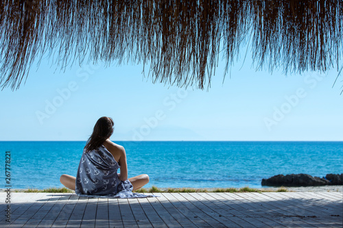 The girl sits on the beach and looks at the sea.
