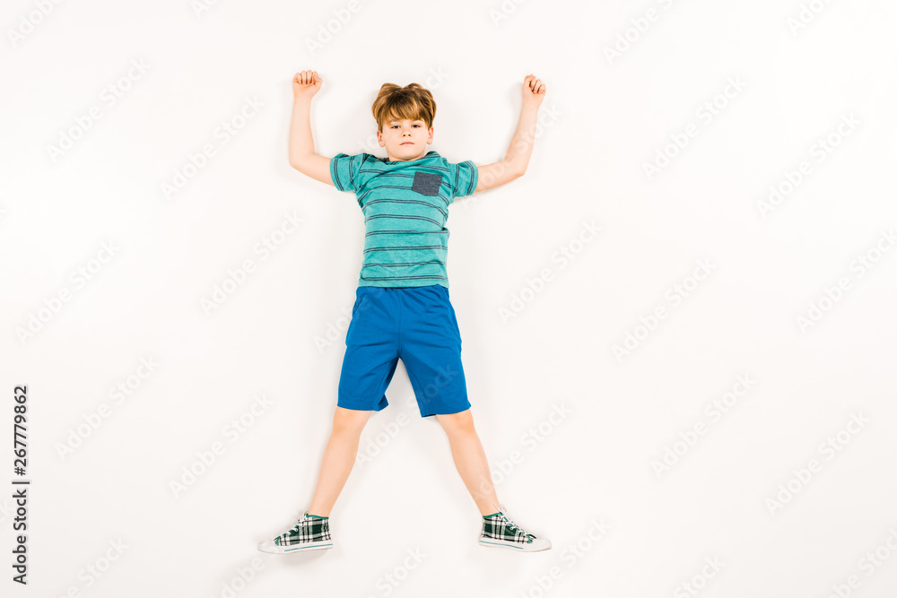top view of cute kid with hands above head looking at camera on white top view of cute kid with hands above head looking at camera on white