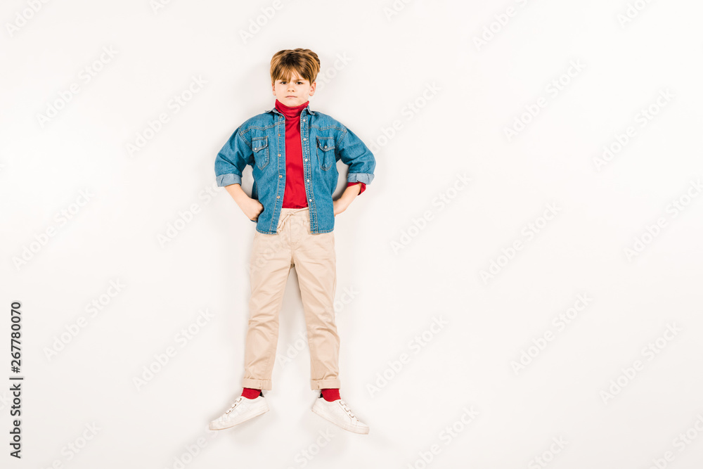 top view of upset kid with hands on hips lying on white top view of upset kid with hands on hips lying on white
