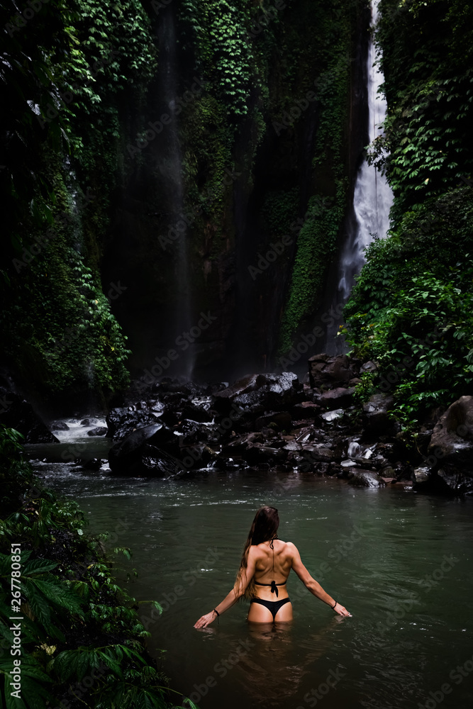 Fototapeta premium Back view of beautiful woman bathing and relaxing in natural swimming pool before waterfall in natural park on tropical island. beautiful waterfall in the Bali, Indinesia