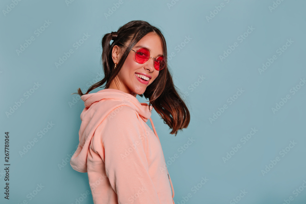 Happy smiling charming girl with dark hair smiling to camera wearing round glasses over blue background Happy smiling charming girl with dark hair smiling to camera wearing round glasses over blue background