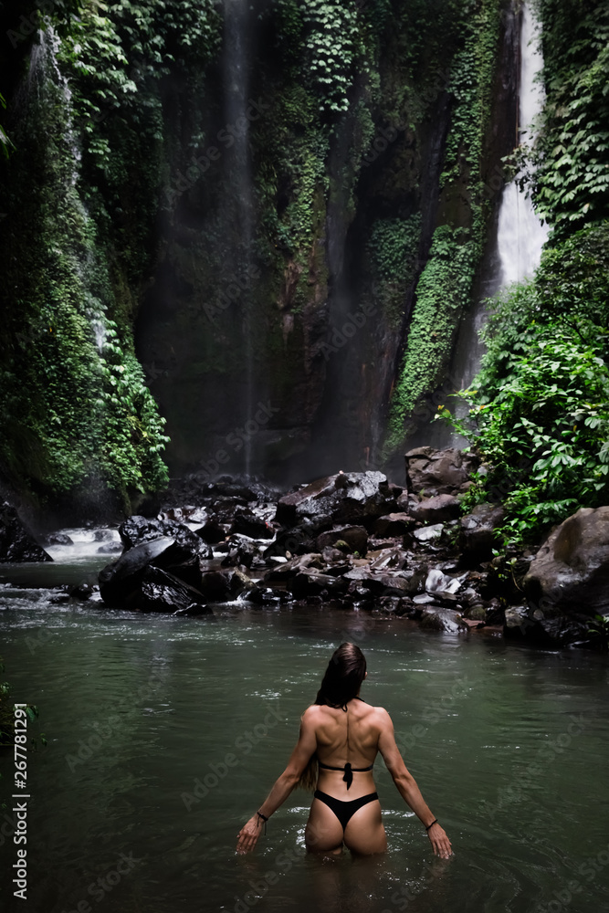 Back view of beautiful woman bathing and relaxing in natural swimming pool before waterfall in natural park on tropical island. beautiful waterfall in the Bali, Indinesia Back view of beautiful woman bathing and relaxing in natural swimming pool before waterfall in natural park on tropical island. beautiful waterfall in the Bali, Indinesia