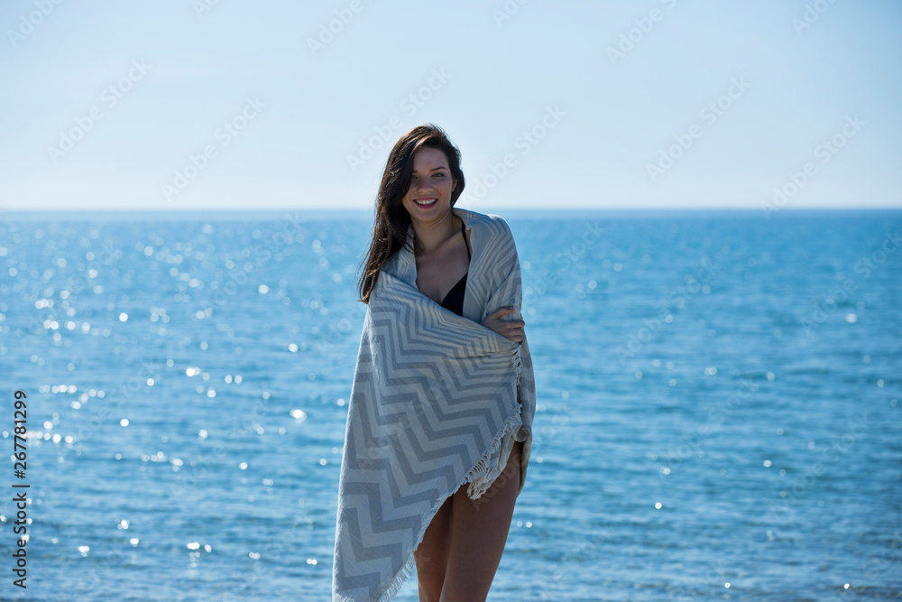 Pretty young girl wrapped in beach towel poses to camera. Full length photo shoot and wonderful hair. Healthy, beauty and summer holiday concept. Pretty young girl wrapped in beach towel poses to camera. Full length photo shoot and wonderful hair. Healthy, beauty and summer holiday concept.