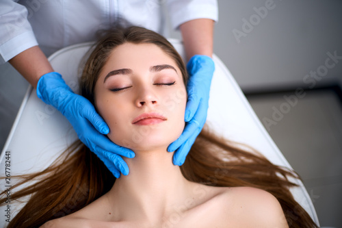 Beautician hands in gloves touching face of attractive woman. Facial Beauty. Beautiful young female with soft smooth healthy skin. Plastic Surgery Concept. Masseur doing relax facial massage at spa.