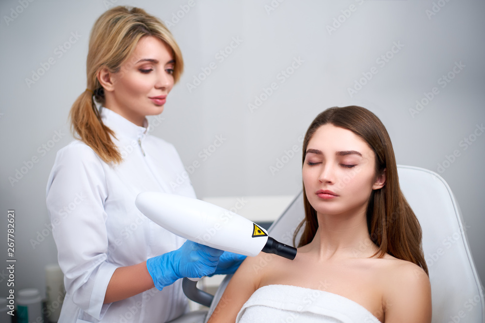 Laser mole removal on a woman's chest in a beauty salon. Hardware cosmetology. Pretty blonde beautician doctor removing birthmark or nevus with laser beam gun in beauty salon. Laser mole removal on a woman's chest in a beauty salon. Hardware cosmetology. Pretty blonde beautician doctor removing birthmark or nevus with laser beam gun in beauty salon.