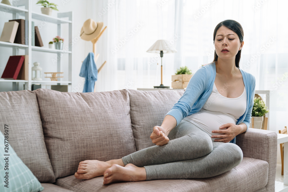 young-asian-pregnant-woman-hands-massaging-swollen-feet-while-sitting