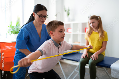 Serious young boy training with sportive rope while doctor photo