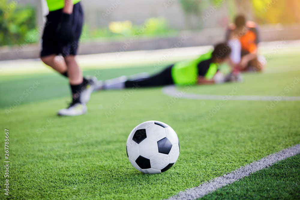 soccer ball on green artificial turf with blurry soccer players standing