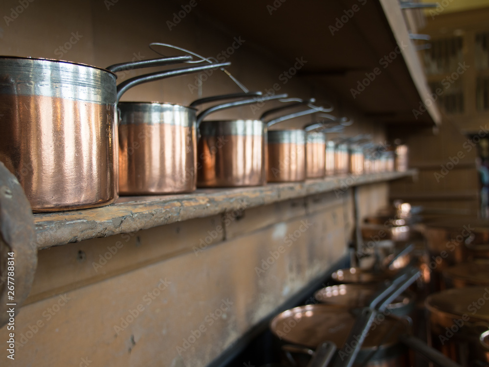 close up of the first of many copper pots in a row on a wooden shelf in an old fashioned kitchen.Focus point on first pot close up of the first of many copper pots in a row on a wooden shelf in an old fashioned kitchen.Focus point on first pot