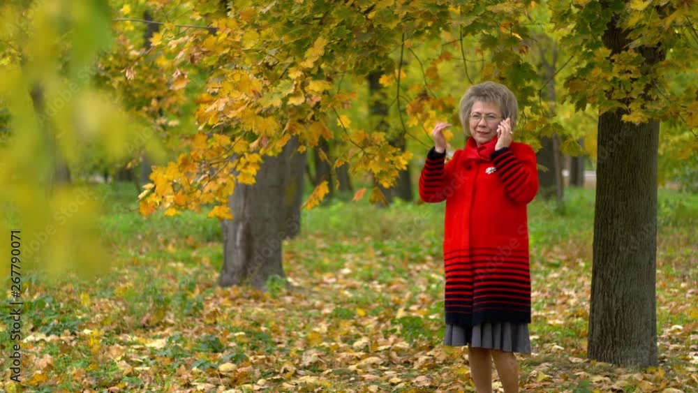 woman in red coat dials a phone number under a tree in autumn park woman in red coat dials a phone number under a tree in autumn park