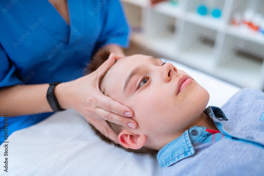 Tranquil short-haired boy calmly lying during relaxing head massage Tranquil short-haired boy calmly lying during relaxing head massage